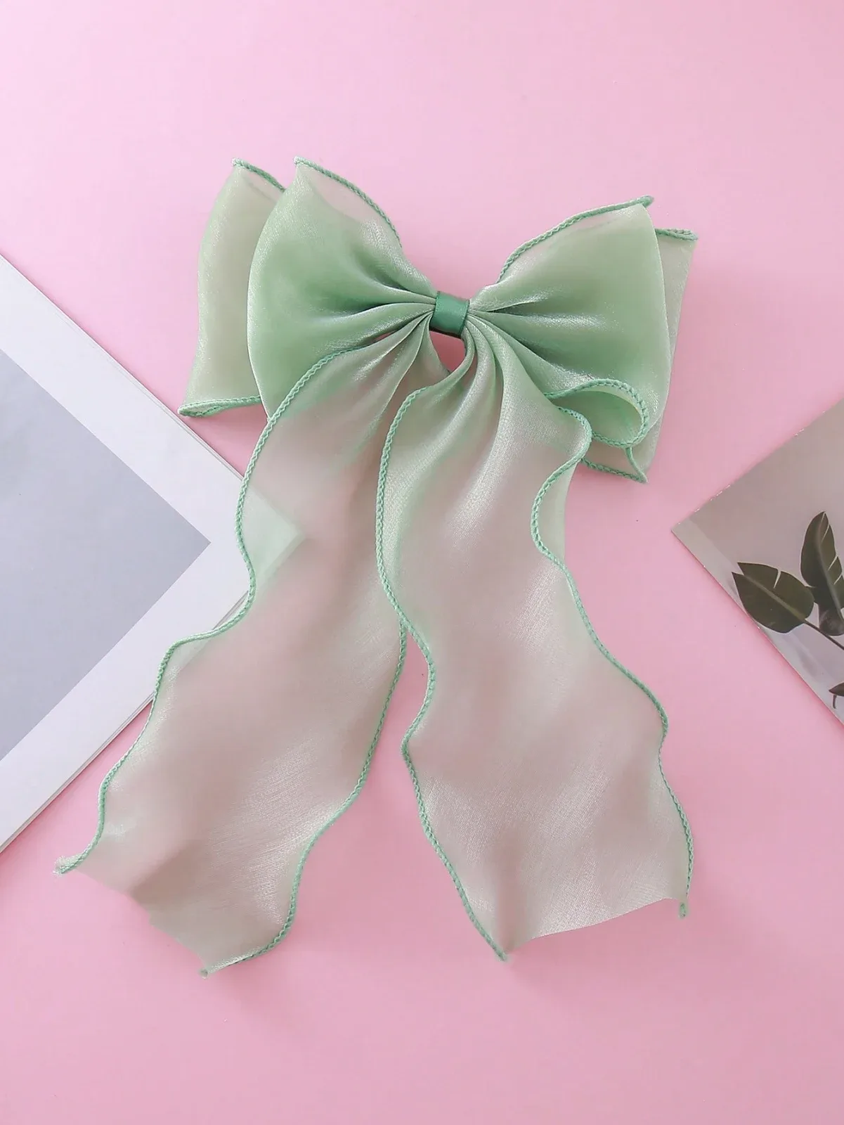 A stylish and soft half-up hair clip with a wavy ribbon in the shape of a large net bow in a refreshing mint green color,